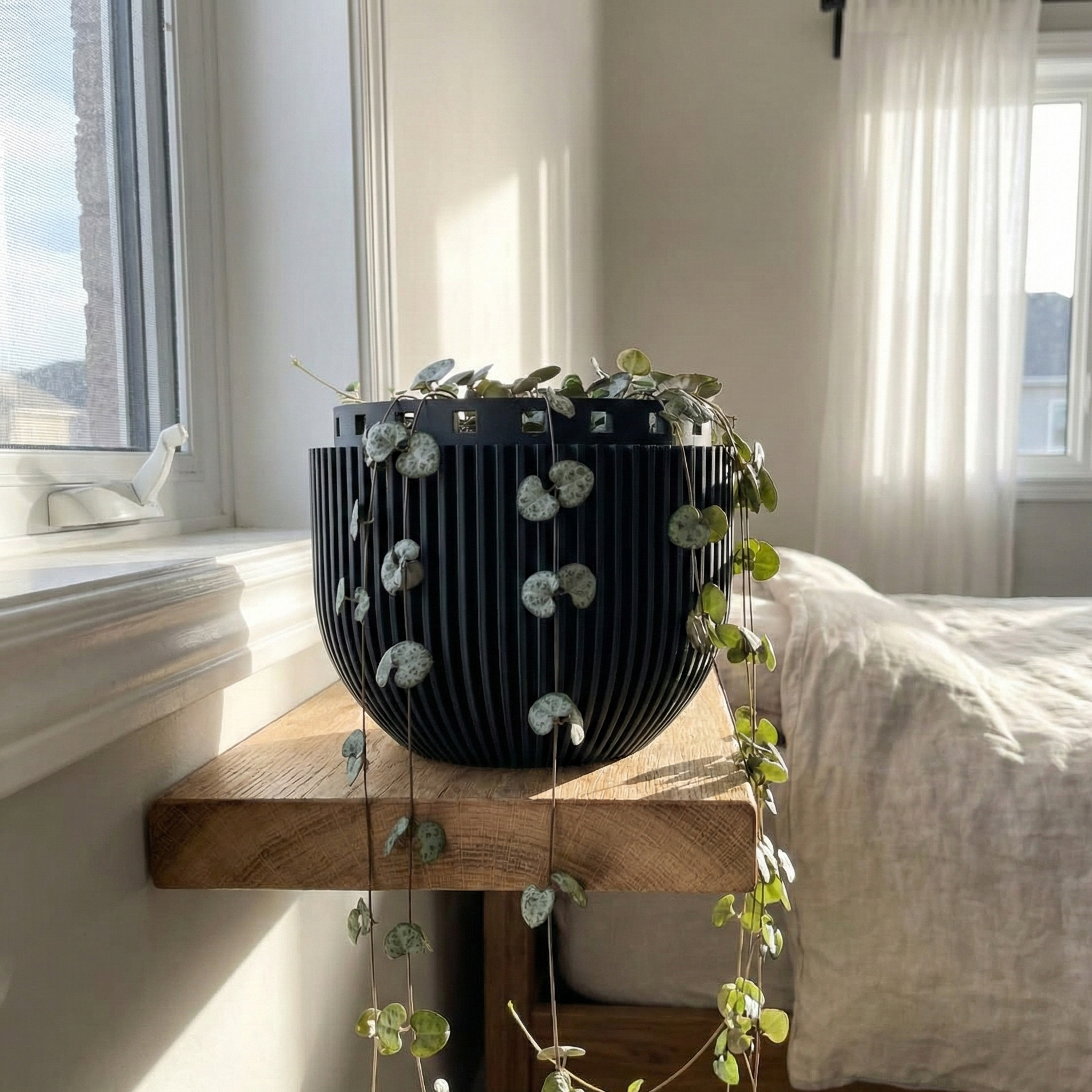 Black decorative vase with greenery on a wooden shelf in a bright bedroom.